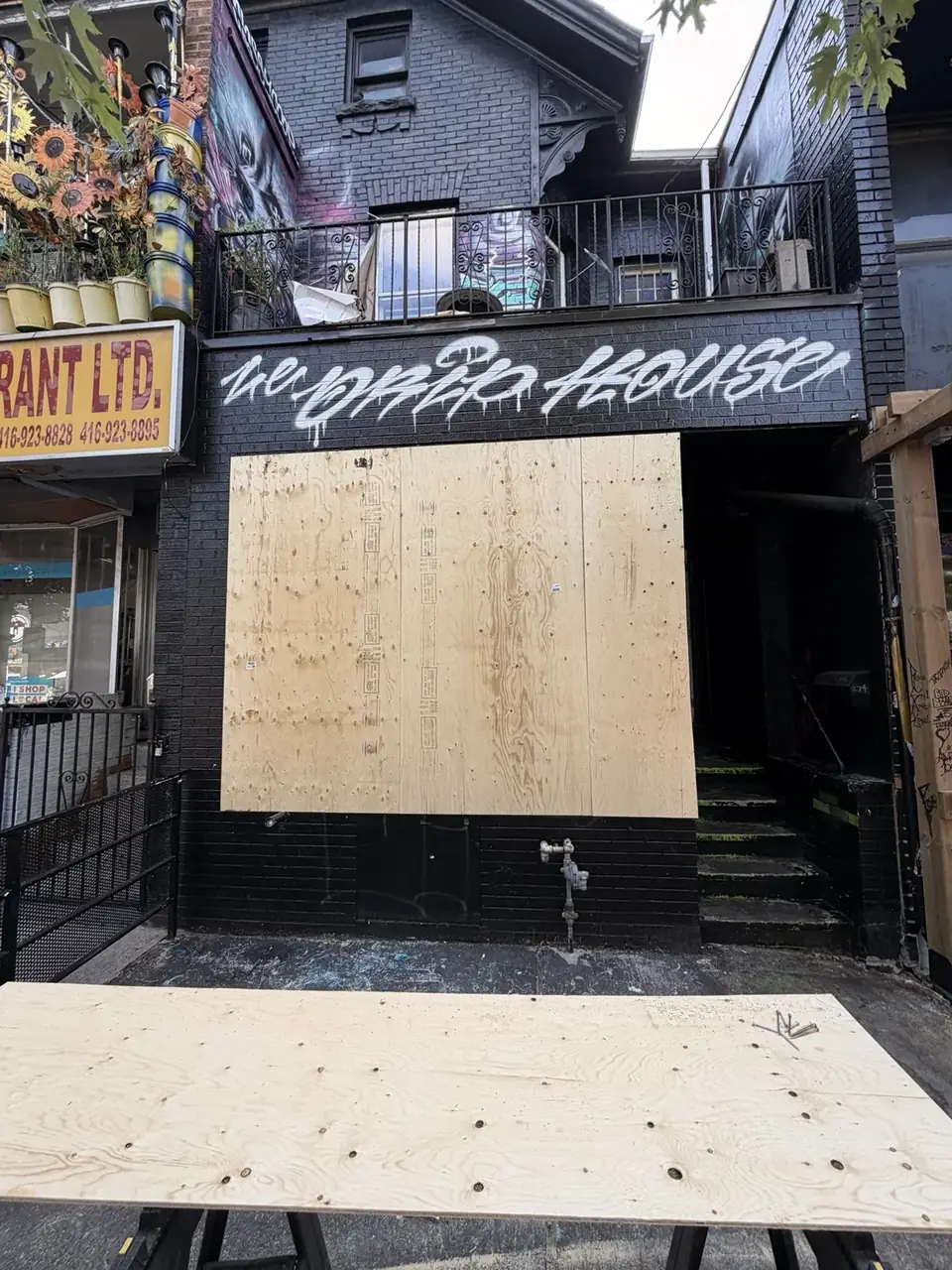 Second view of emergency plywood board-up securing a broken storefront in Kensington Market, Toronto