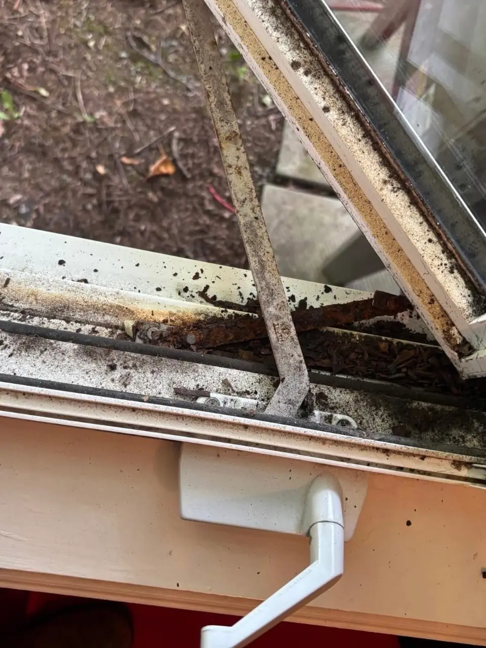 Rusted casement window hardware with corroded 2-bar hinge, operating arm and track near Humberwood Park, Toronto
